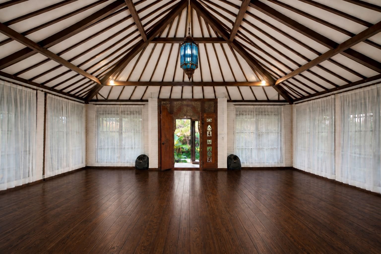 Brahma Shala in daylight: timber floor, white curtains on every wall, a blue lantern hanging from the peaked roof