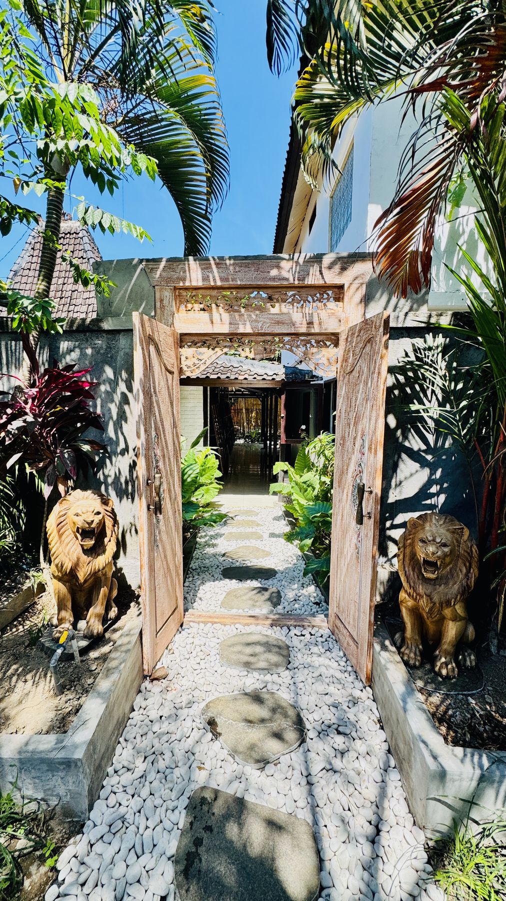 Two carved stone lions guarding an old timber door, with a garden path beyond