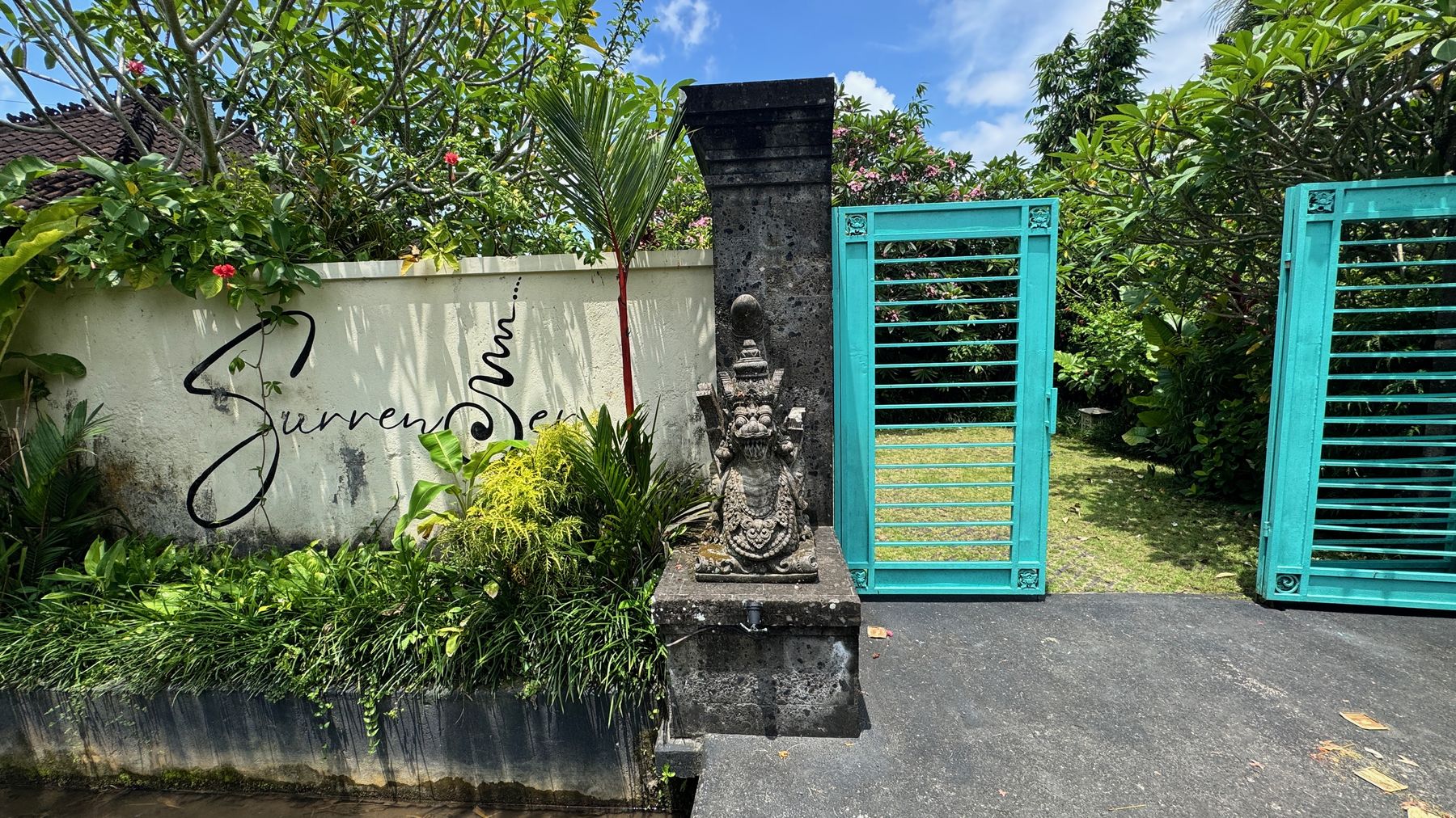 The entrance: a stone wall with Surrender written in script, beside a teal gate and garden