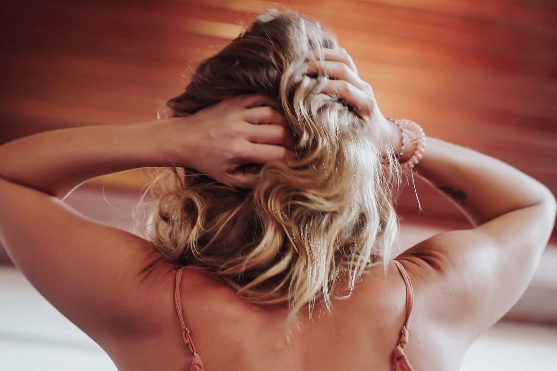 A woman from behind, hands lifted into her hair, in warm red light