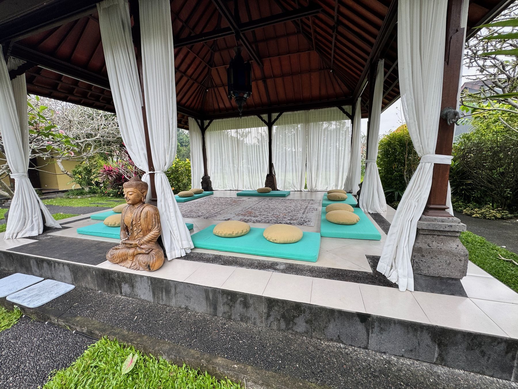 Kali Shala, an open-air pavilion in the garden with white curtains tied at each post and cushions laid in a circle