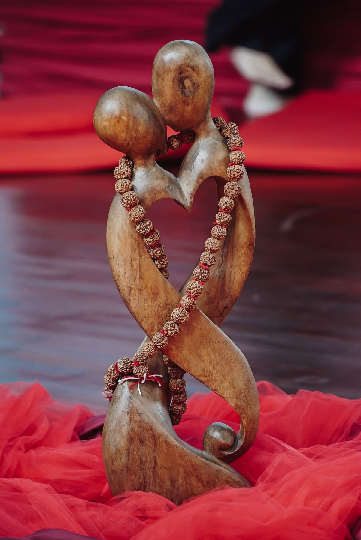 A carved wooden sculpture of two entwined figures wrapped in prayer beads, lit red